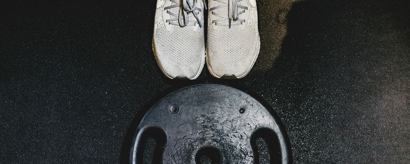 Running shoes beside a weight plate on a dark gym floor